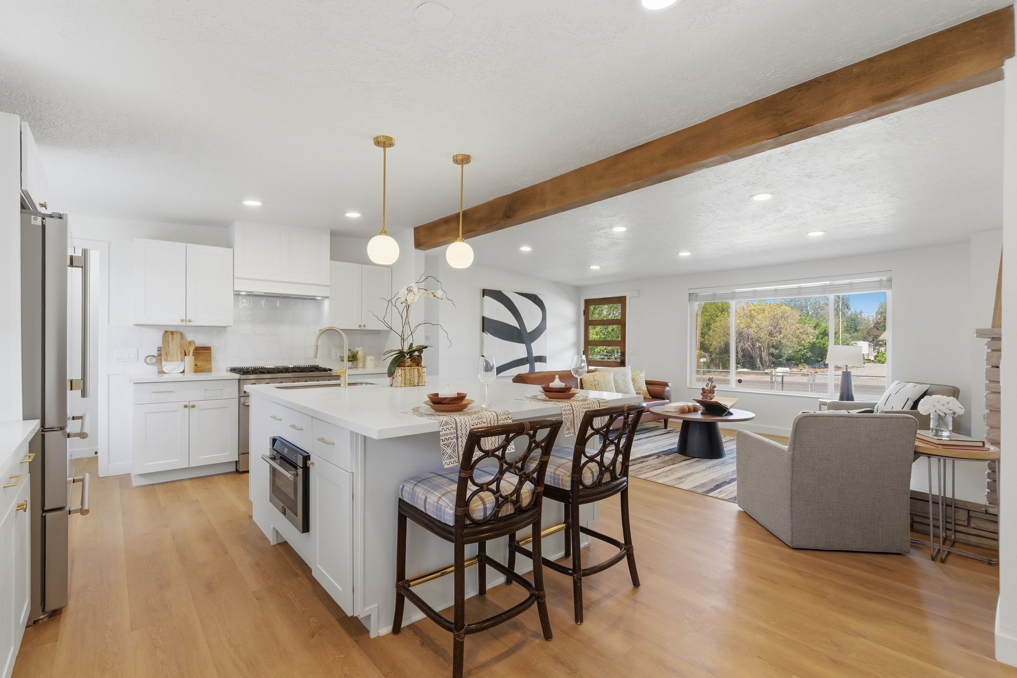 Open-concept living space featuring a central kitchen island with seating, a large picture window, wood-finish flooring, recessed lighting, and an exposed ceiling beam