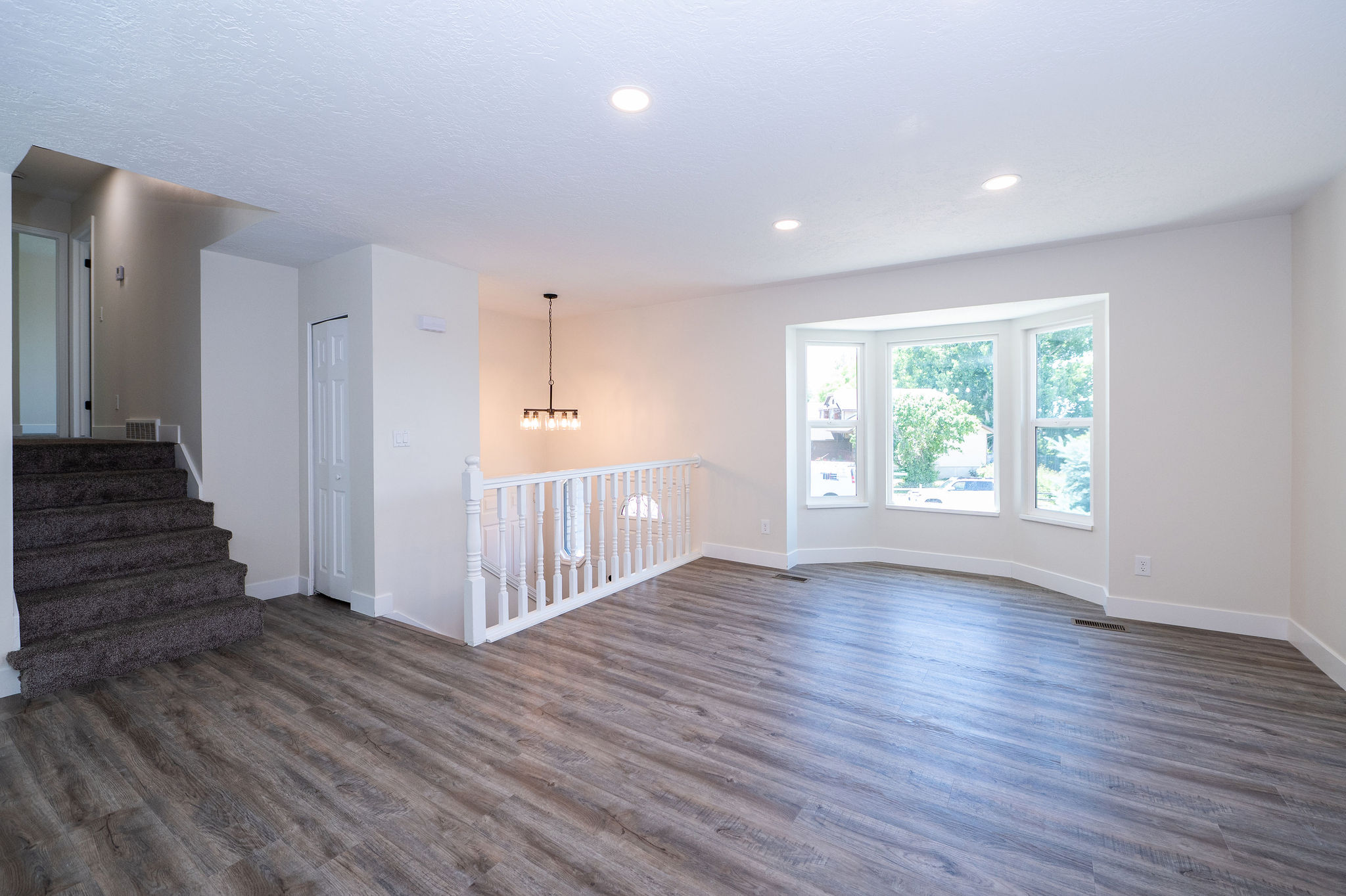 Spacious living area featuring wood-finish flooring, a bay window, recessed lighting, and a contemporary chandelier
