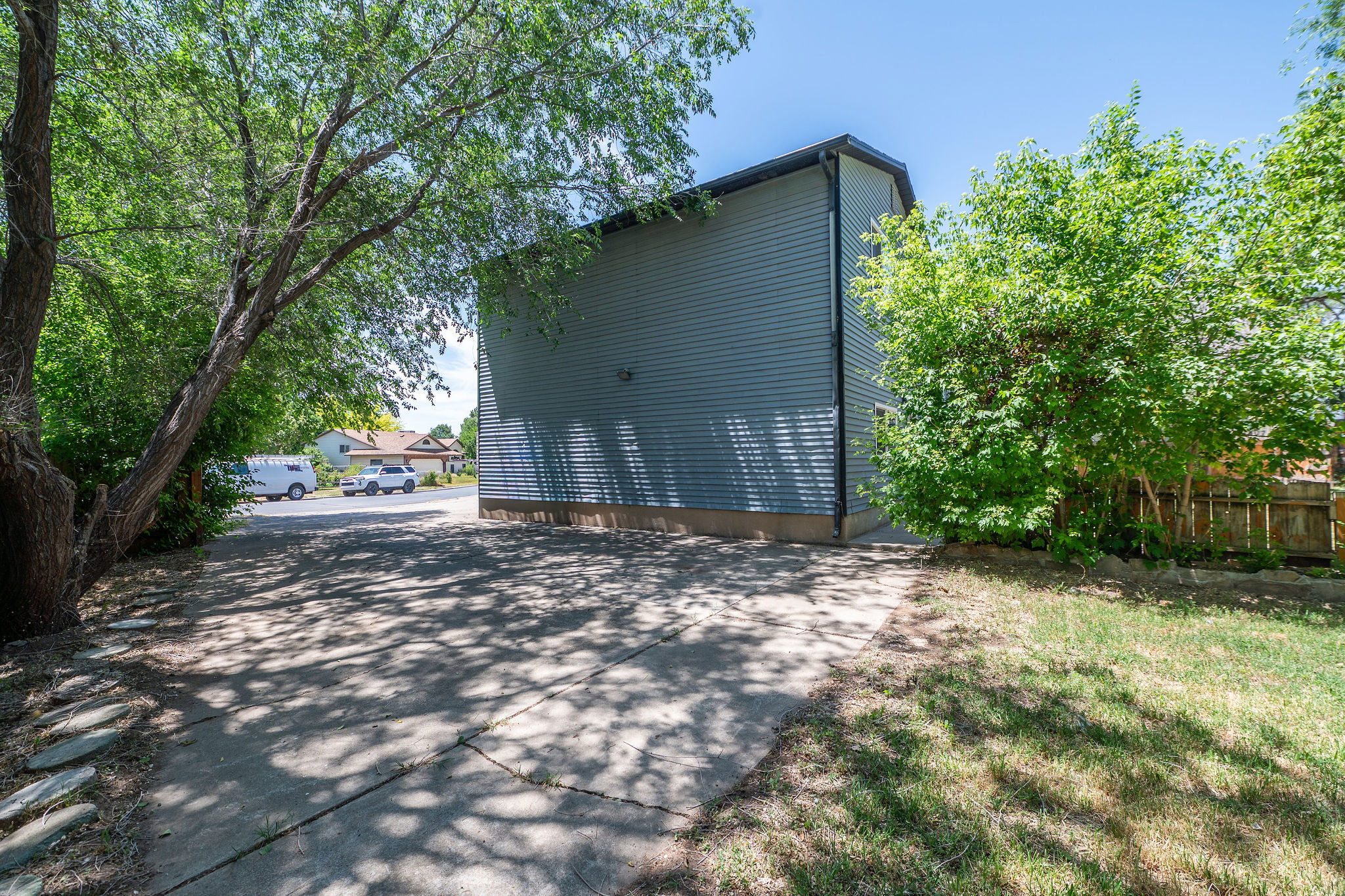 Exterior featuring blue horizontal siding, a concrete driveway, mature trees, and established shrubbery