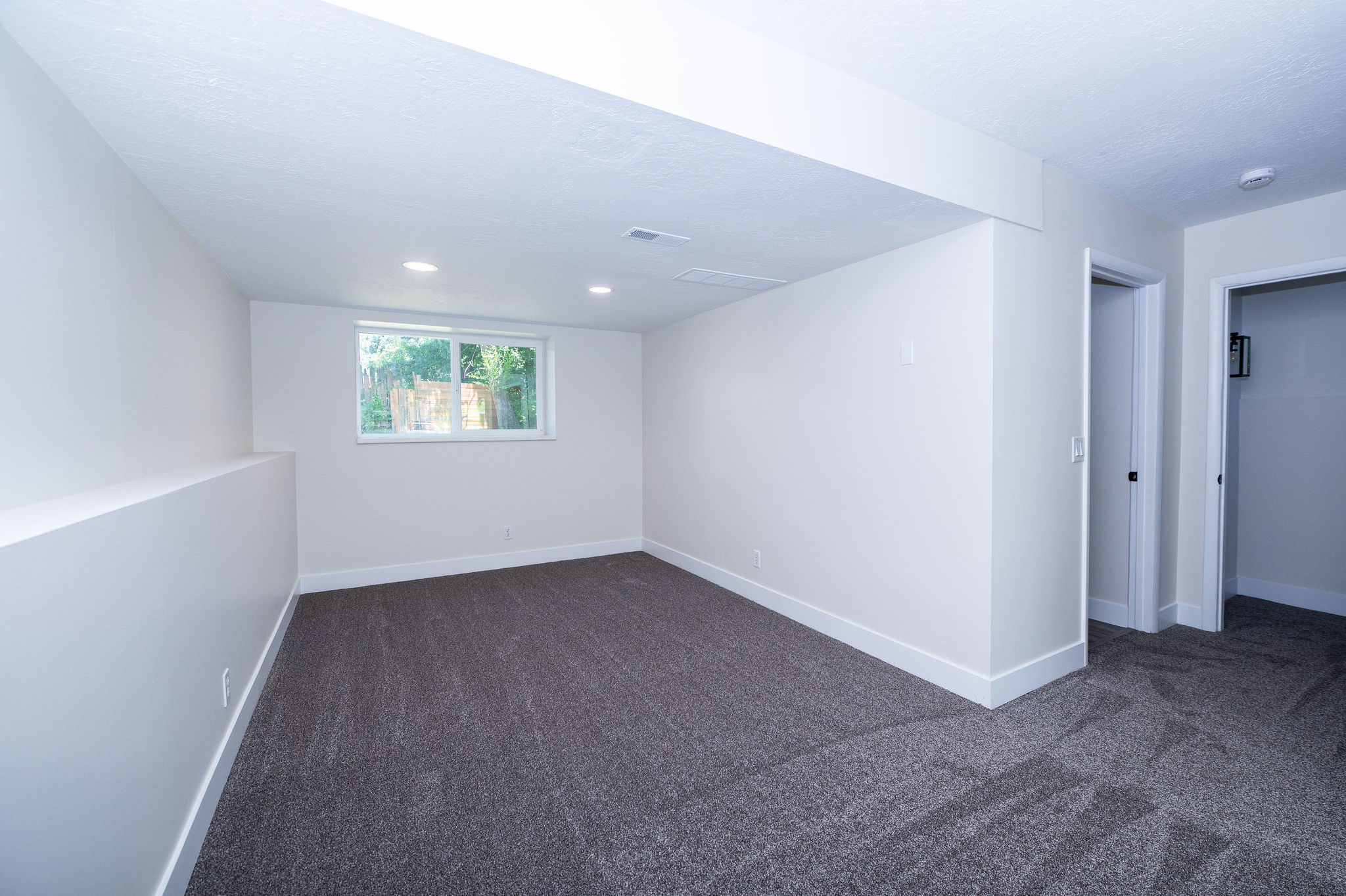 Spacious room featuring neutral carpeting, recessed lighting, and a window providing natural illumination