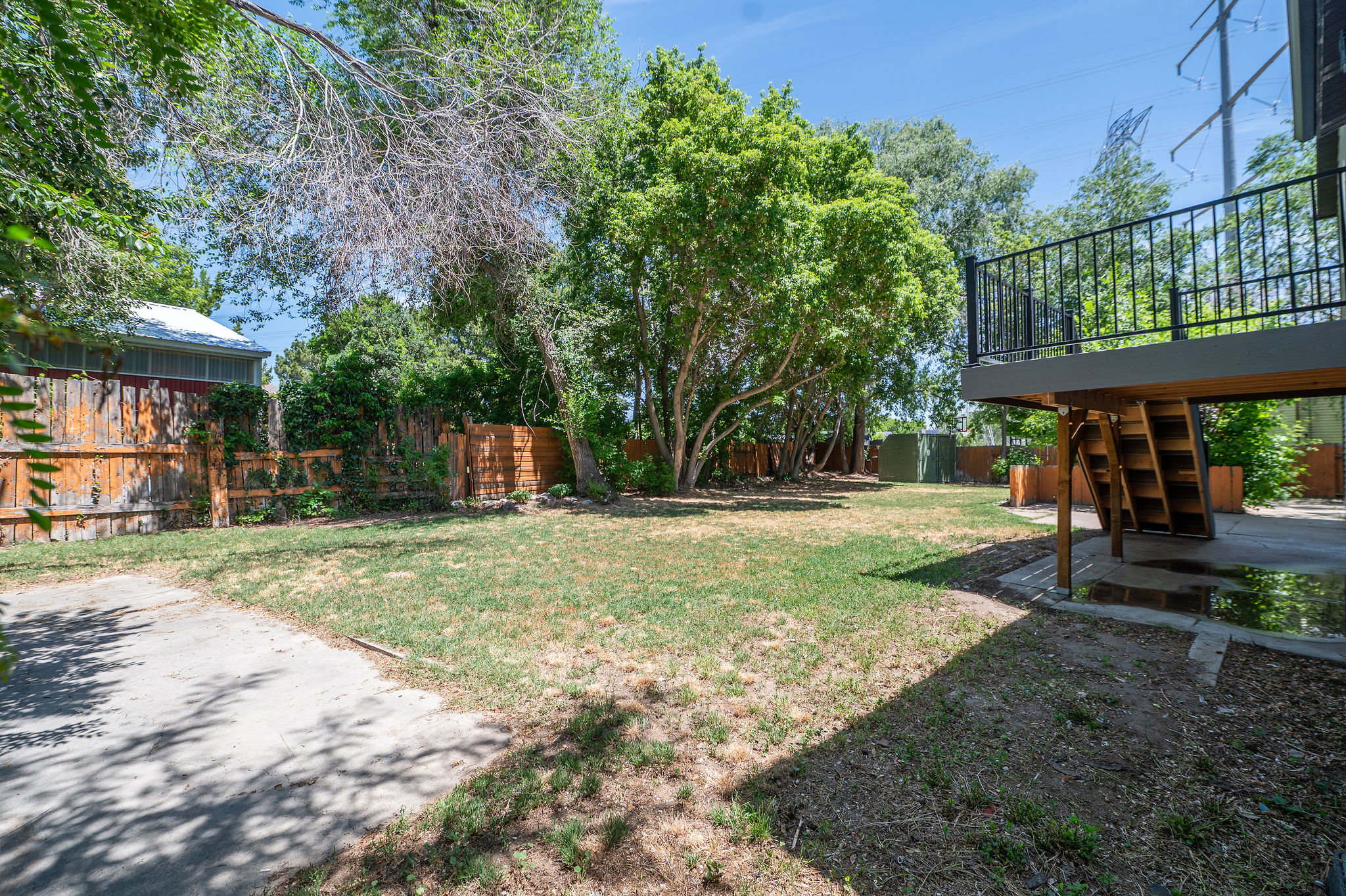 Expansive yard featuring a wooden privacy fence, mature trees, and a raised exterior deck with metal railings and staircase