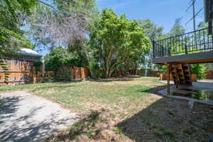 Expansive yard featuring a wooden privacy fence, mature trees, and a raised exterior deck with metal railings and staircase