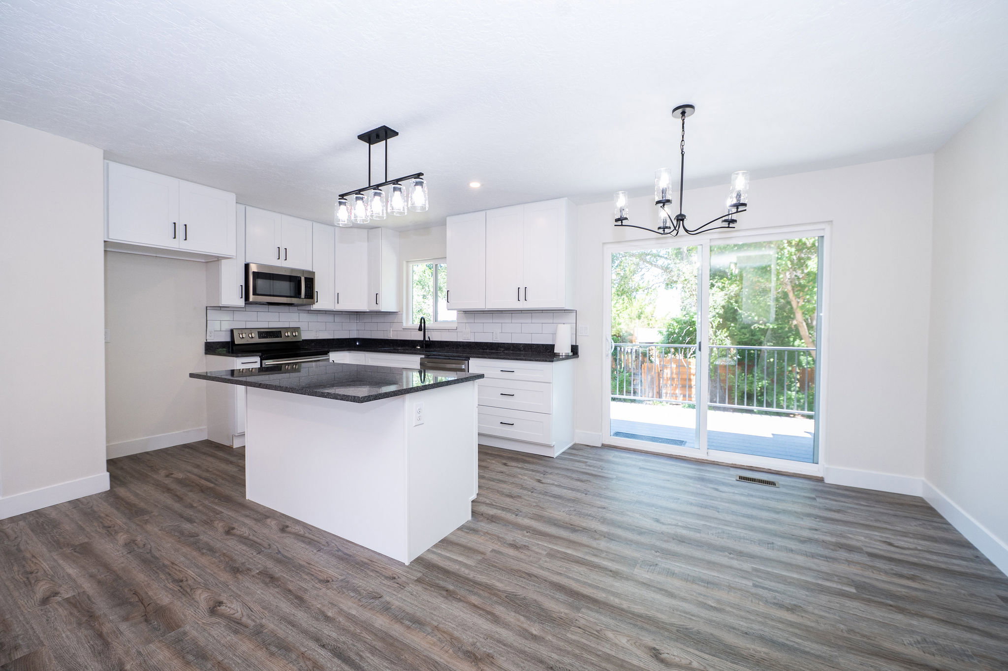 Modern kitchen featuring an island with a dark countertop, white cabinetry with dark hardware, stainless steel appliances, and wood-finish flooring
