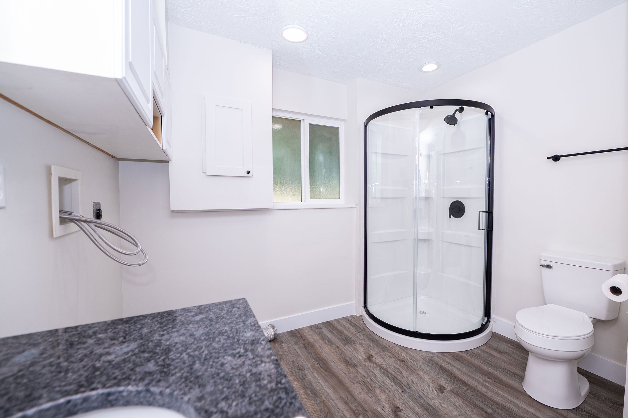 Bathroom featuring a corner shower with dark-framed glass enclosure, white toilet, and wood-finish flooring