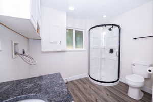 Bathroom featuring a corner shower with dark-framed glass enclosure, white toilet, and wood-finish flooring