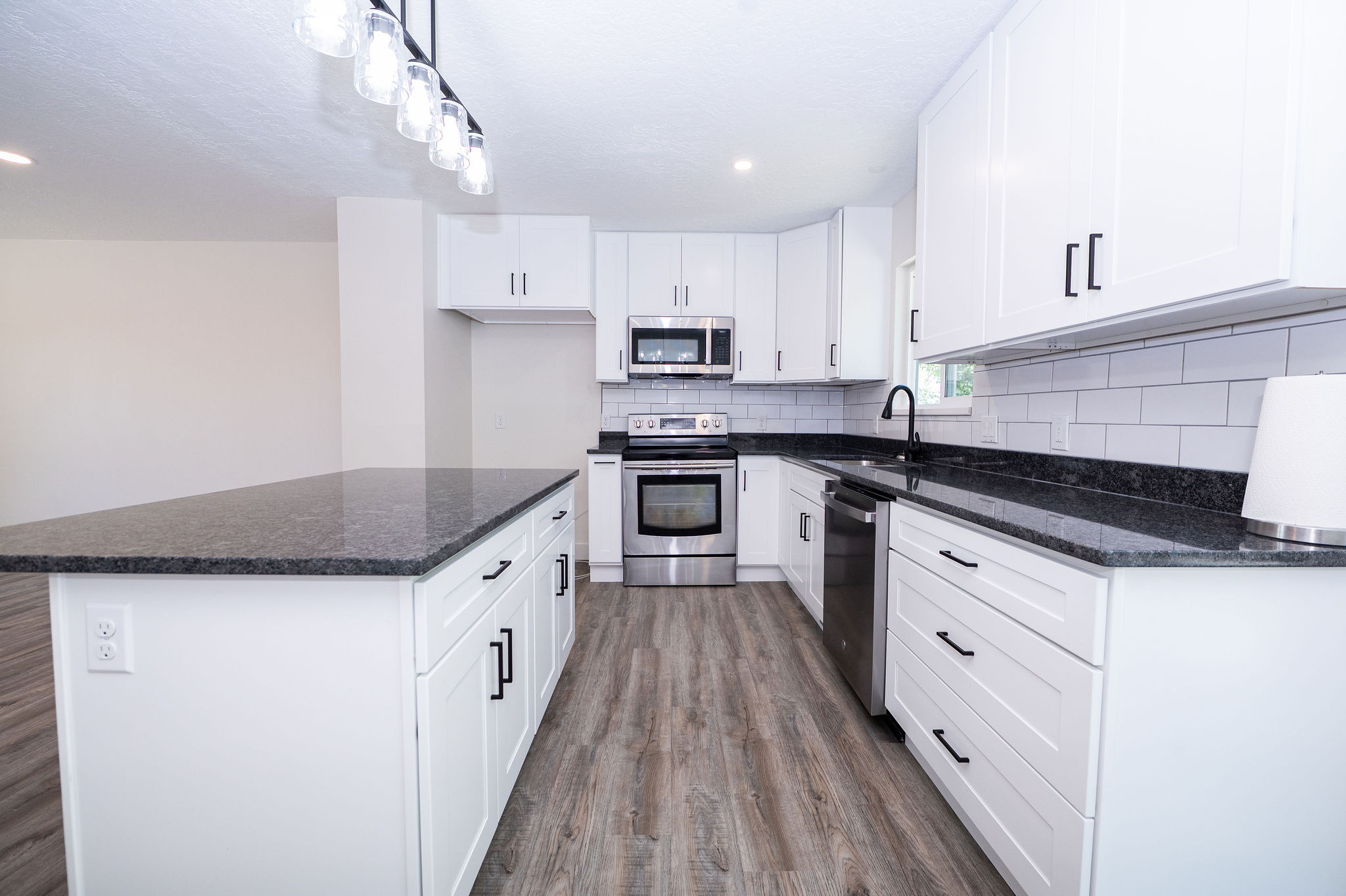 Kitchen featuring a central island with a dark countertop, white shaker-style cabinetry, stainless steel appliances, subway tile backsplash, and wood-finish flooring