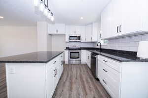Kitchen featuring a central island with a dark countertop, white shaker-style cabinetry, stainless steel appliances, subway tile backsplash, and wood-finish flooring