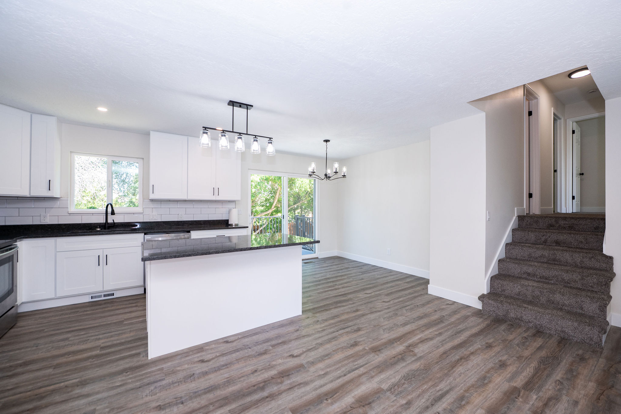Contemporary kitchen featuring white cabinetry, dark countertops, a subway tile backsplash, stainless steel appliances, and a central island