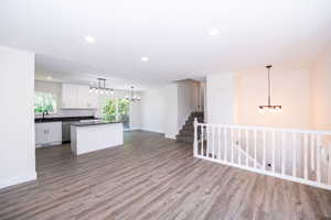 Open-concept living area featuring wood-finish flooring, a contemporary kitchen with white cabinetry and dark countertops, a kitchen island, and a white baluster railing