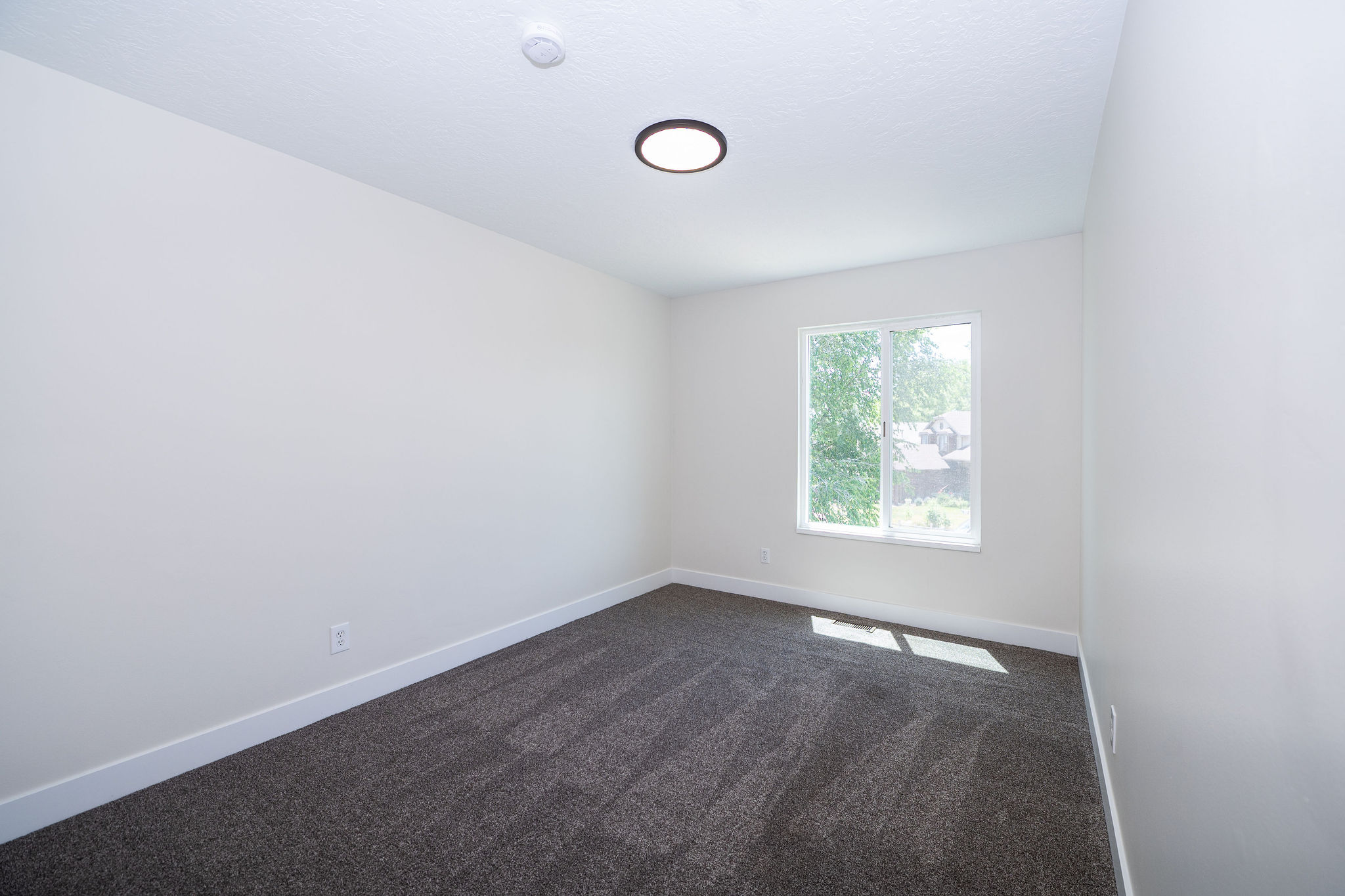 Bedroom featuring light-toned walls, dark gray carpet, a white framed window, and a circular ceiling light fixture