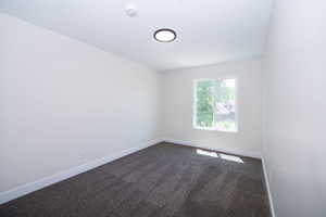 Bedroom featuring light-toned walls, dark gray carpet, a white framed window, and a circular ceiling light fixture