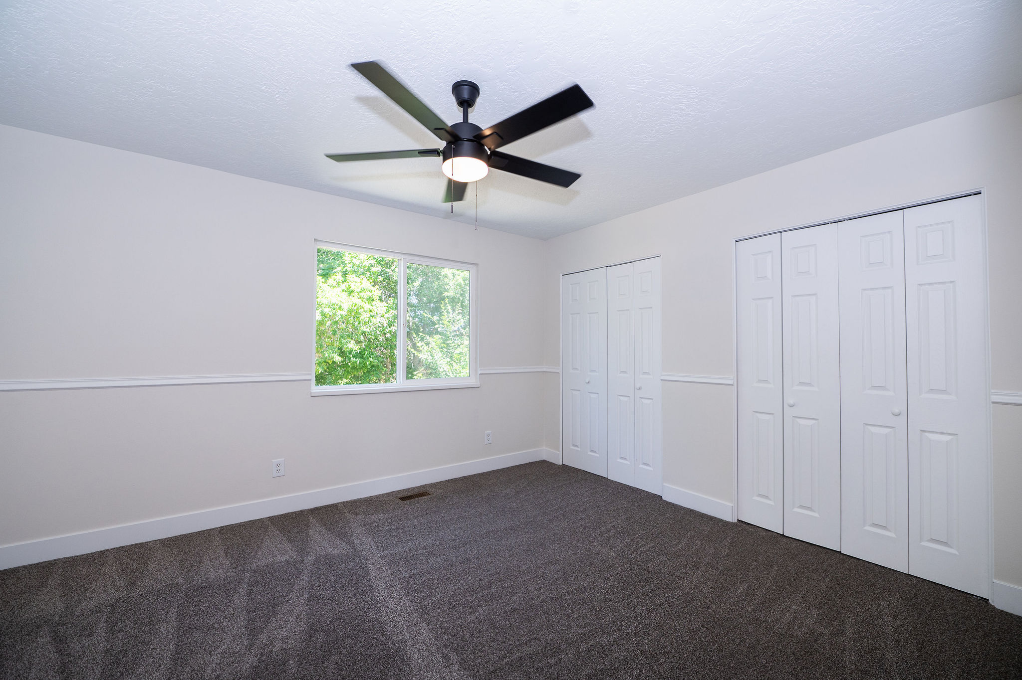 Bright interior space featuring a double window, dark patterned carpet, and a modern ceiling fan