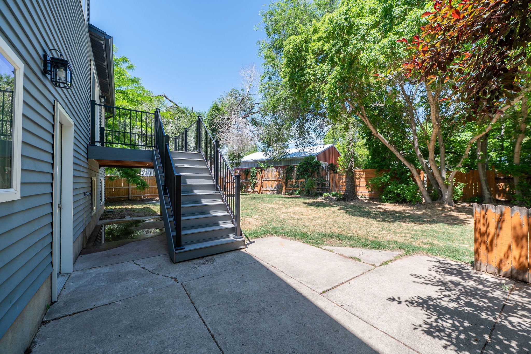 Exterior features a gray siding facade with a black iron railing leading to an upper-level deck