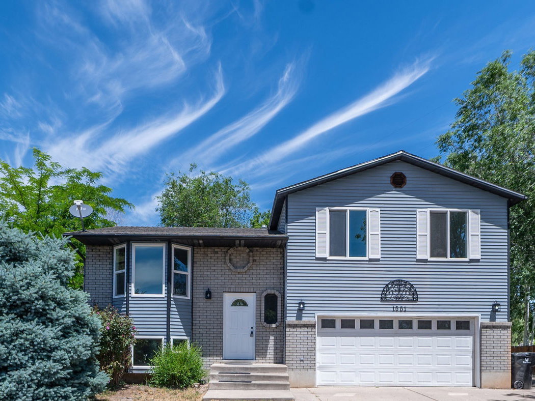 Split-level residence featuring gray siding, a white front door, and a two-car garage