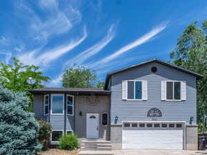 Split-level residence featuring gray siding, a white front door, and a two-car garage