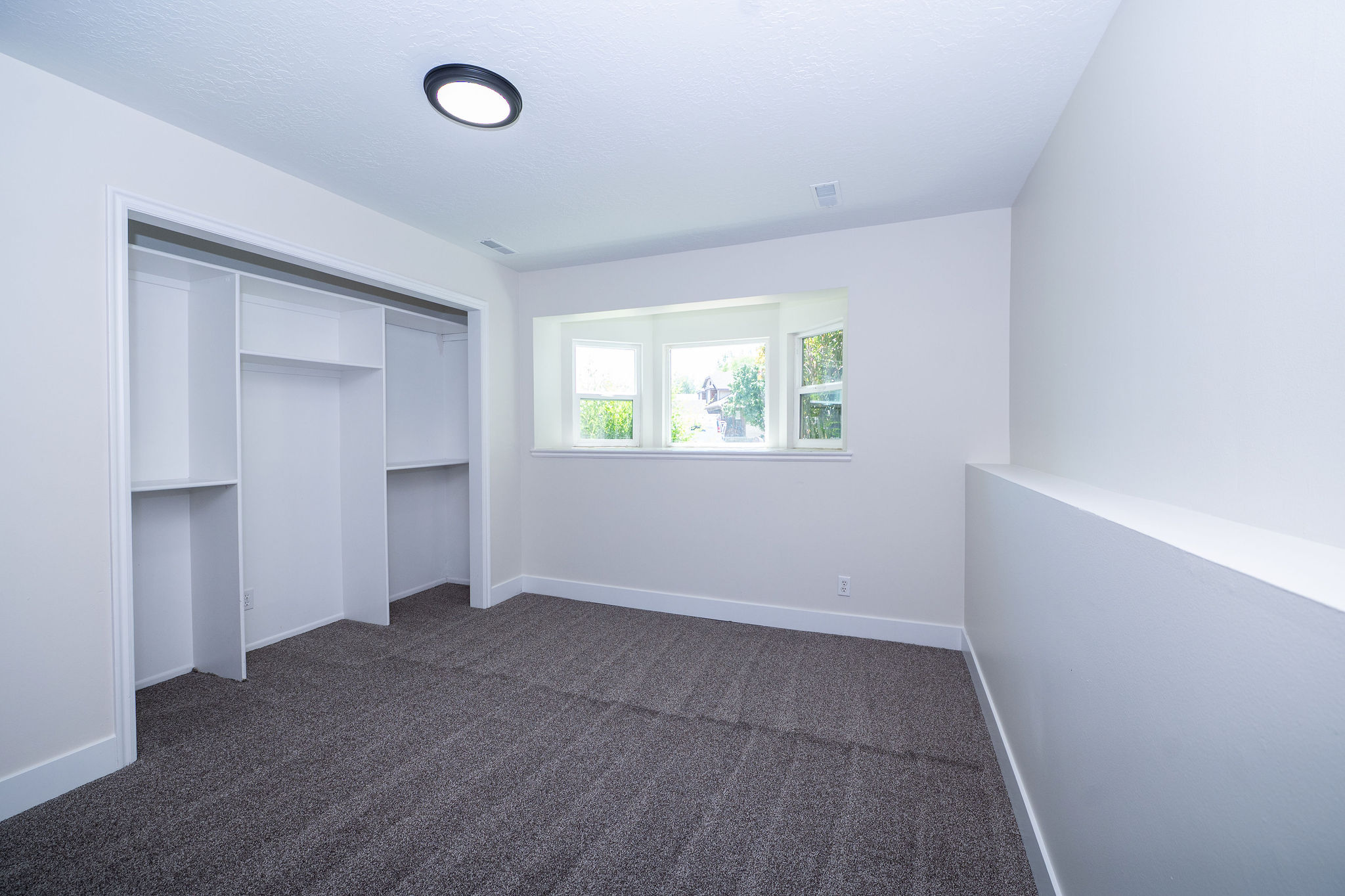 Room featuring textured gray carpeting, a built-in closet with shelving, a recessed window, white walls, and a contemporary flush-mount ceiling light fixture