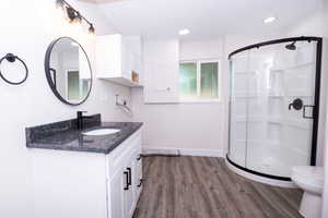 Bathroom featuring a curved glass shower enclosure, white vanity with a dark speckled countertop, black fixtures, and wood-finish flooring
