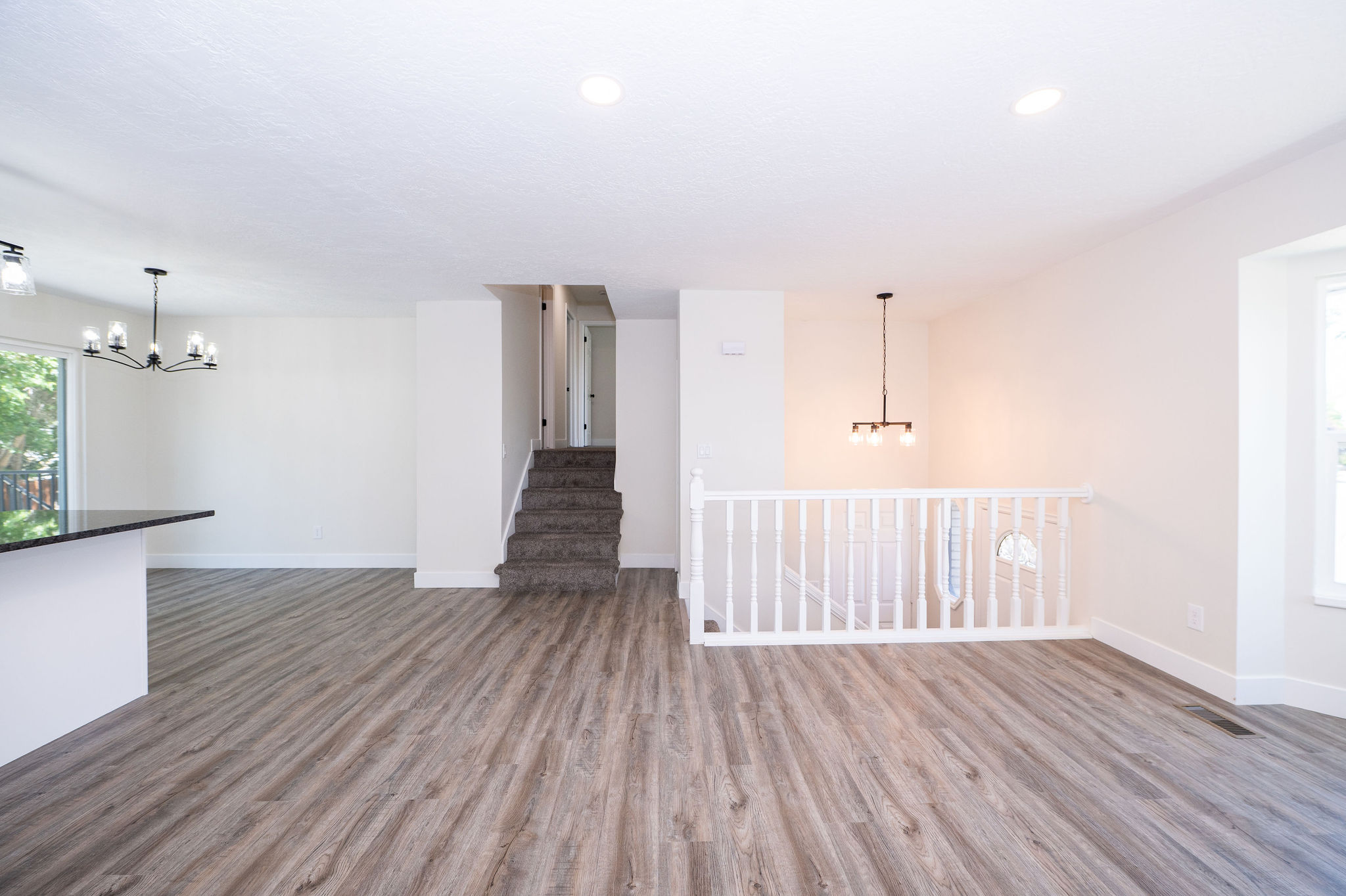 Open-concept living area featuring wood-finish flooring, recessed lighting, and a modern black chandelier