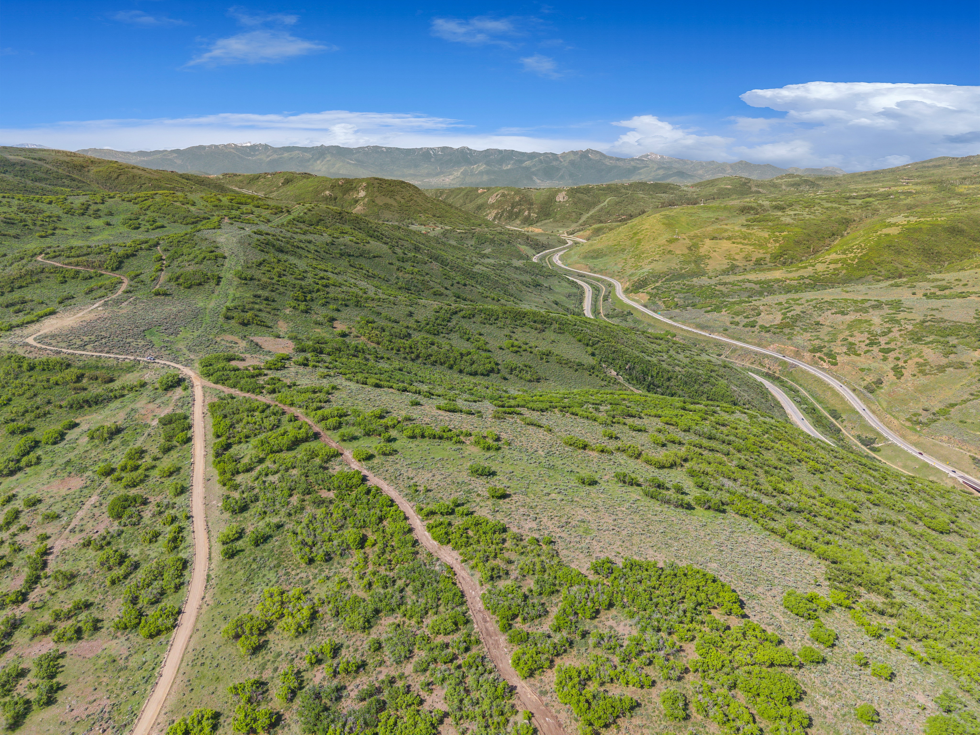 Expansive mountainous terrain featuring winding roads and verdant foliage under a blue sky