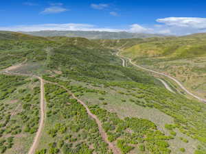 Expansive mountainous terrain featuring winding roads and verdant foliage under a blue sky