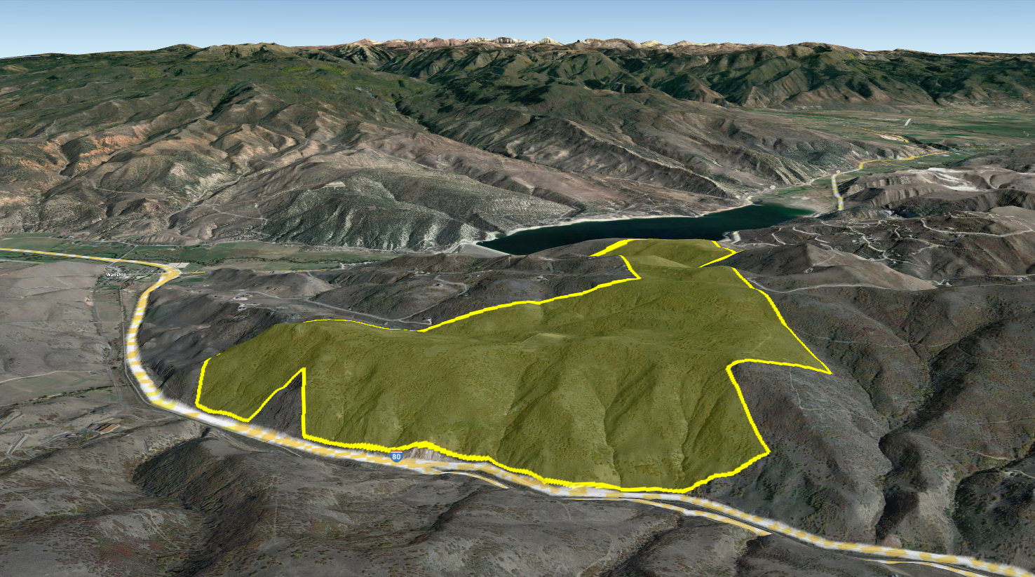 Expansive land parcel outlined in yellow, featuring varied topography with hills and valleys, roadside frontage, and distant mountain ranges