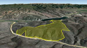 Expansive land parcel outlined in yellow, featuring varied topography with hills and valleys, roadside frontage, and distant mountain ranges