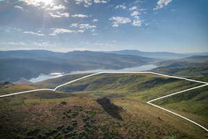 Expansive undeveloped land with a white boundary overlay, featuring rolling hills and distant mountainous terrain