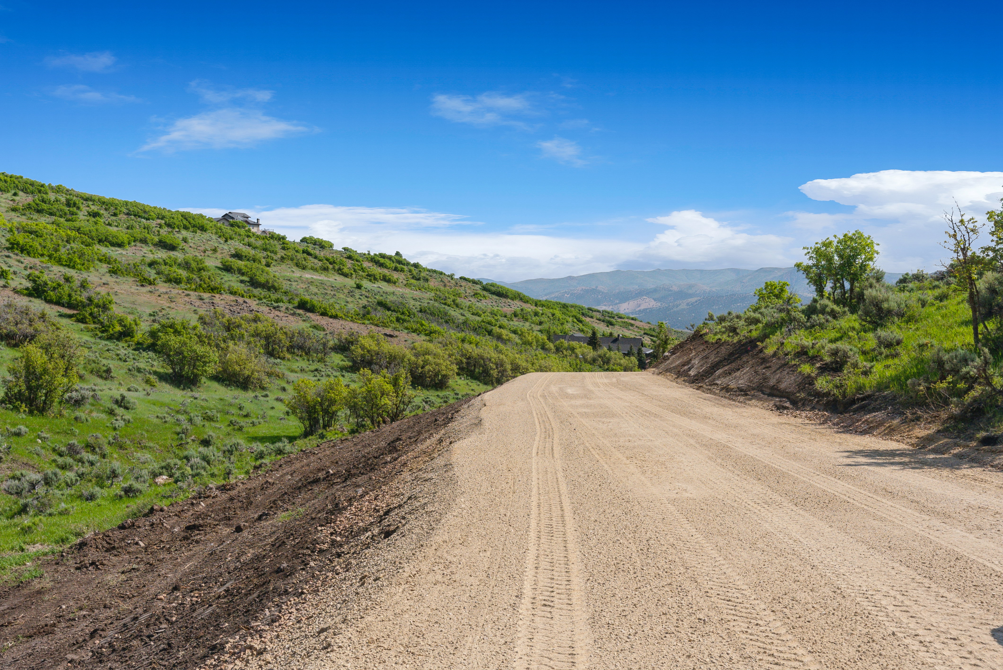 Expansive graded dirt road traversing a hillside with natural vegetation