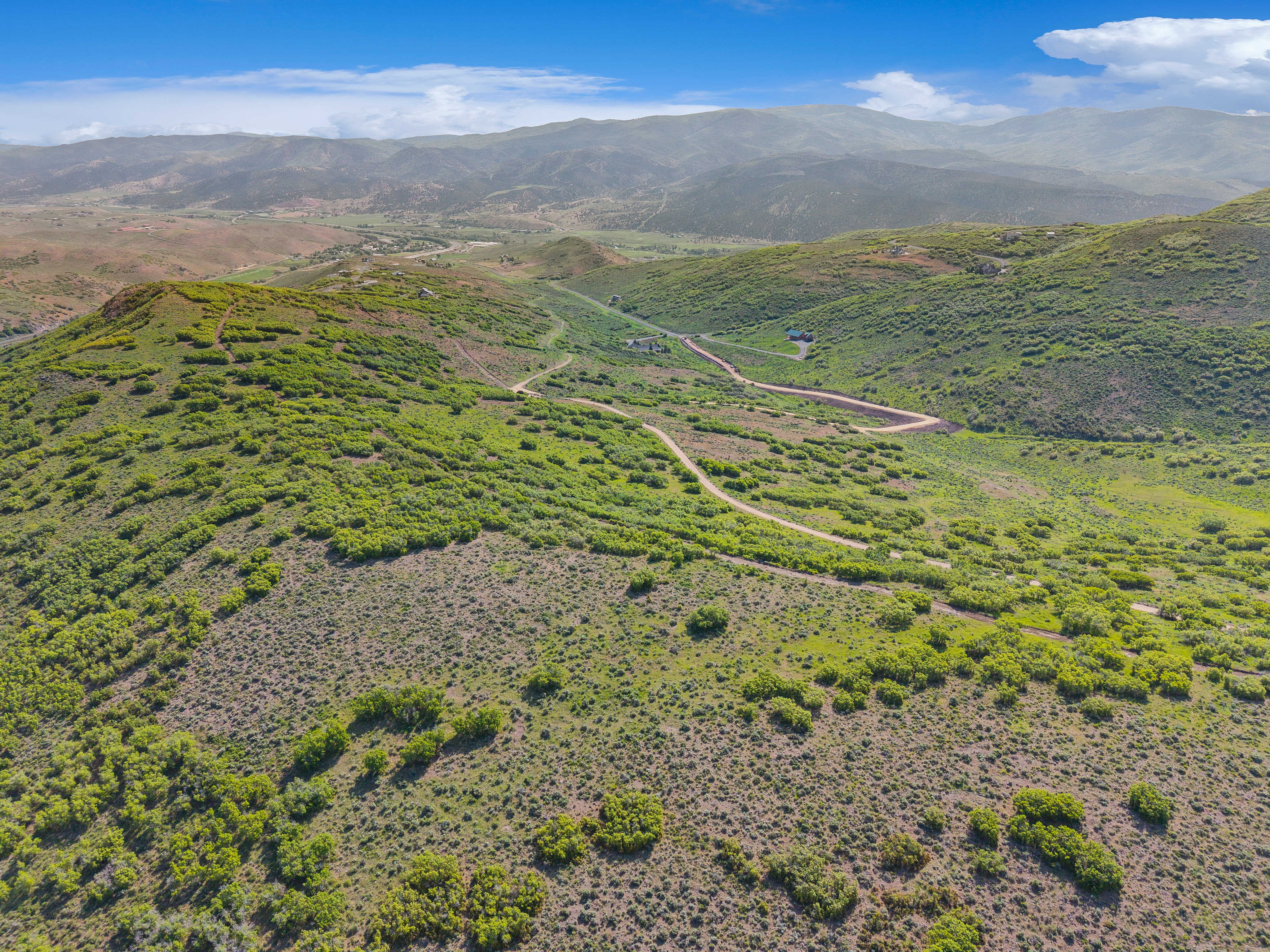 Expansive mountainous terrain featuring natural vegetation, distant structures, and visible roadways