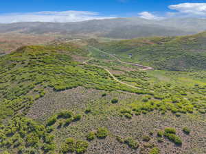 Expansive mountainous terrain featuring natural vegetation, distant structures, and visible roadways