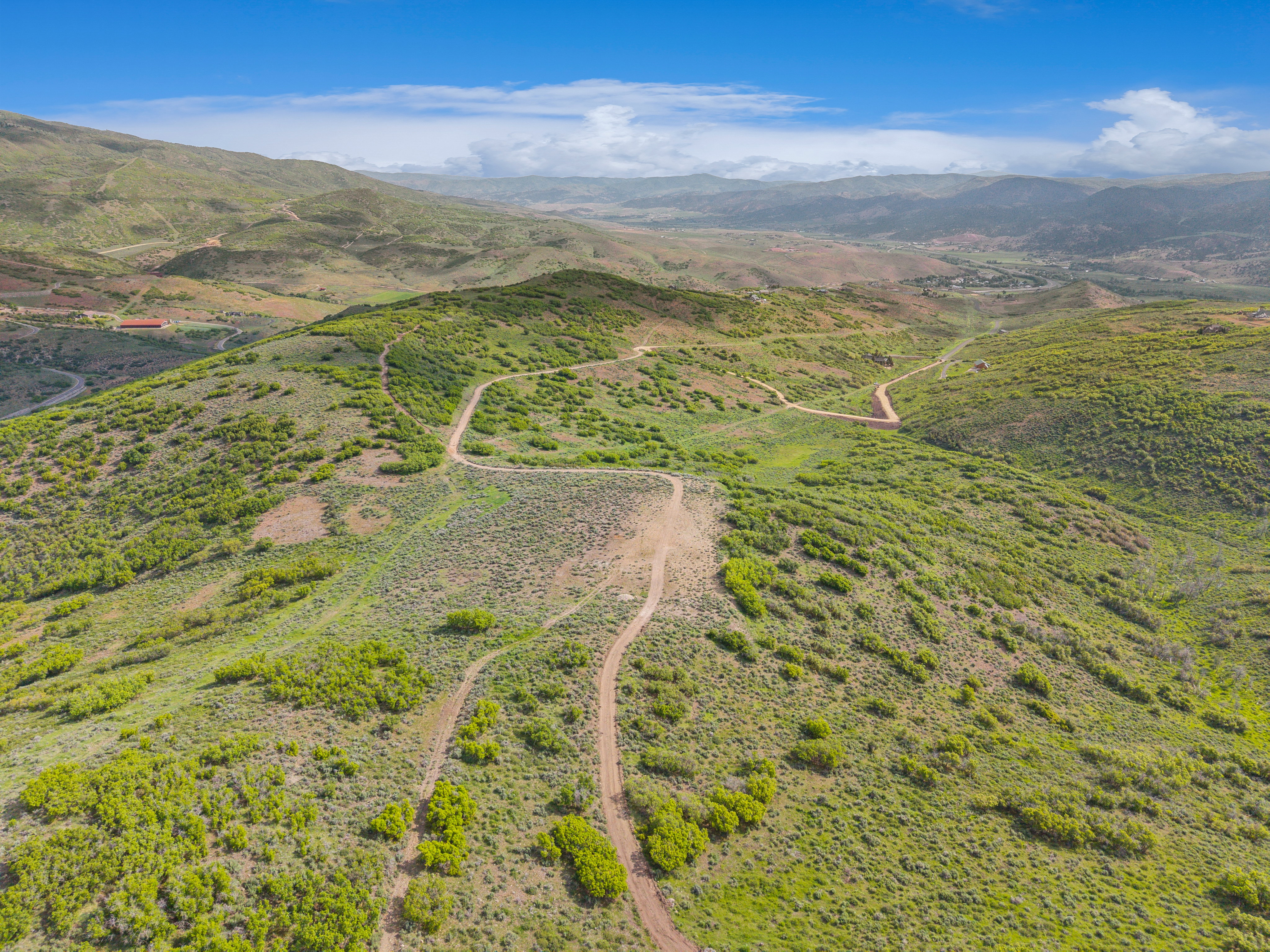 Expansive, undulating terrain featuring verdant shrubbery and visible dirt paths