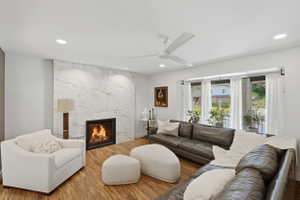 Living area featuring a modern linear fireplace with a full-height stone surround, wood-finish flooring, recessed lighting, a ceiling fan, and a wide window with multiple panes