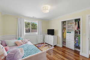 Bedroom featuring wood-finish flooring, a double-pane window, and white crown molding