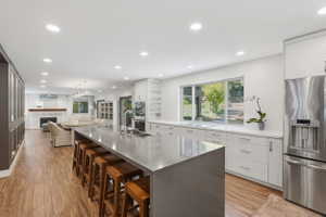 Open-concept kitchen featuring an expansive island with seating, stainless steel appliances, white cabinetry, and recessed lighting