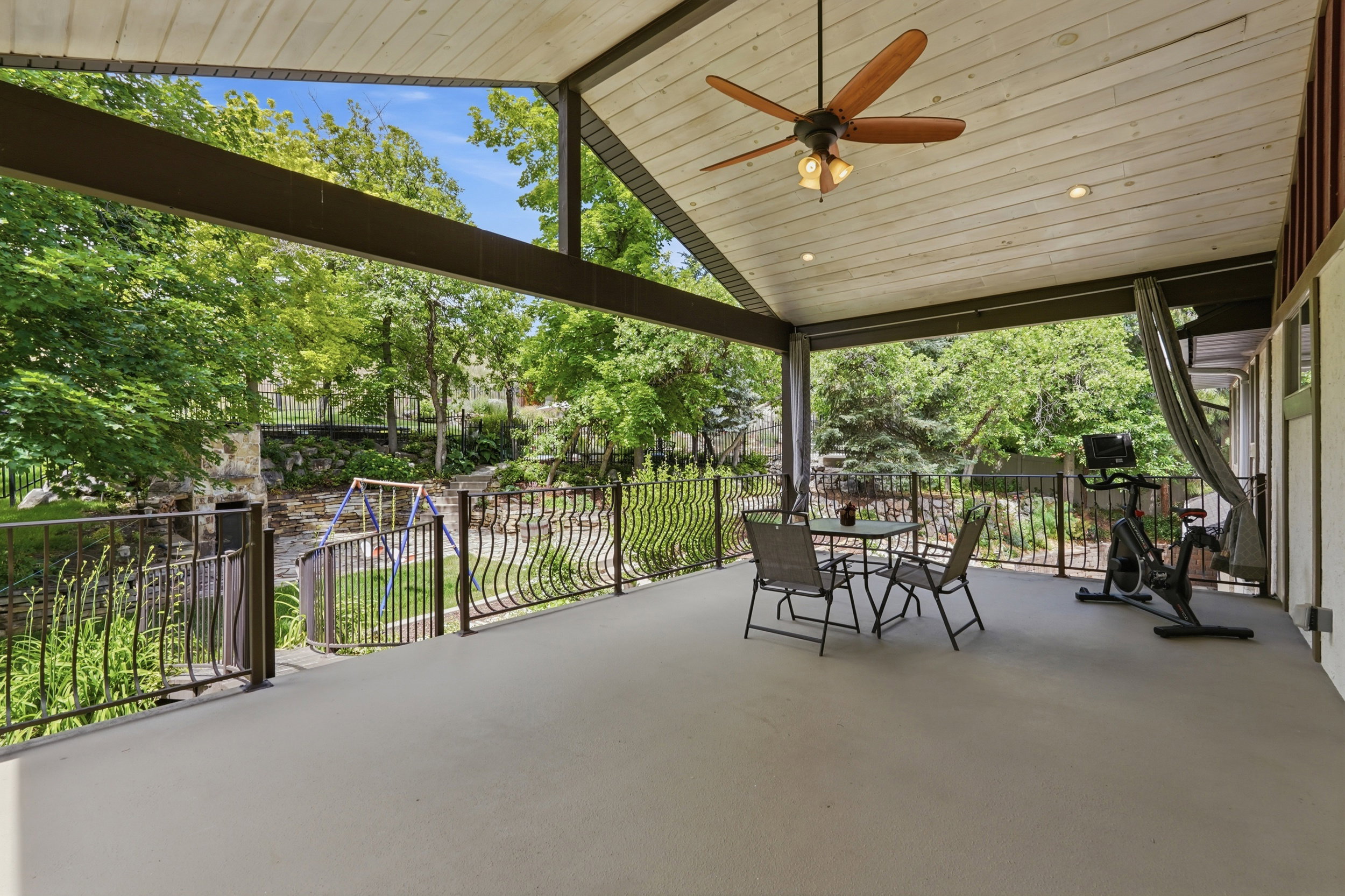Spacious covered patio featuring a vaulted wood-finish ceiling, ceiling fan, recessed lighting, and ornate metal railings