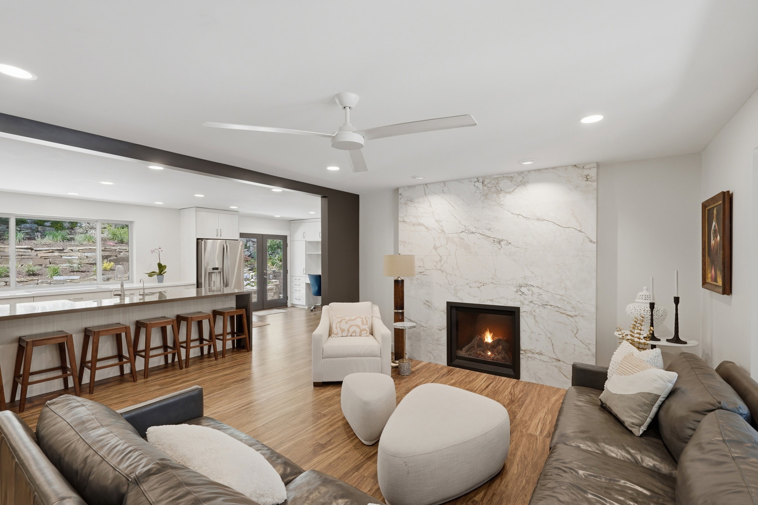 Open-concept living space featuring wood-finish flooring, a contemporary fireplace with a stone surround, and recessed lighting