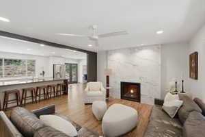 Open-concept living space featuring wood-finish flooring, a contemporary fireplace with a stone surround, and recessed lighting