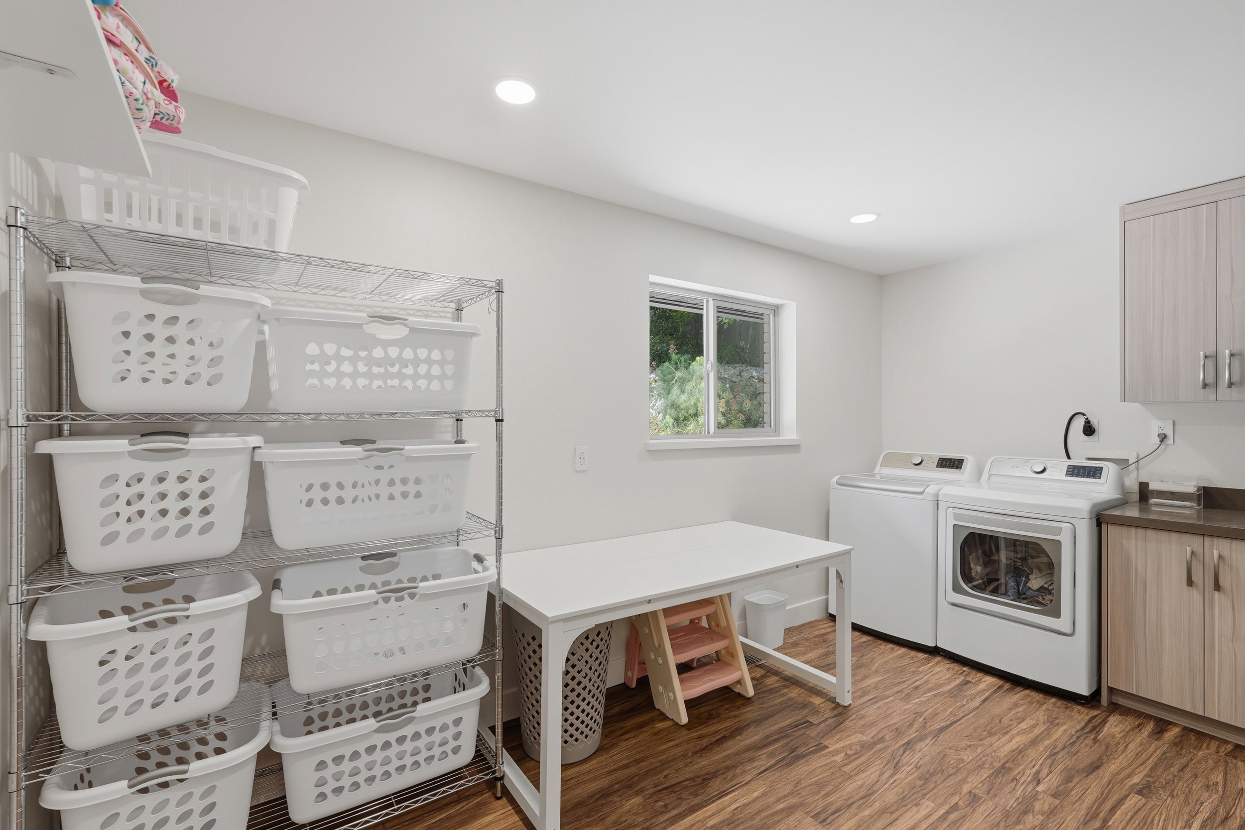 Dedicated laundry area featuring wood-finish flooring, a window providing natural light, recessed ceiling lighting, and built-in cabinetry with a countertop