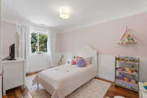 Interior room with hardwood-finish flooring, white crown molding, and white wainscoting