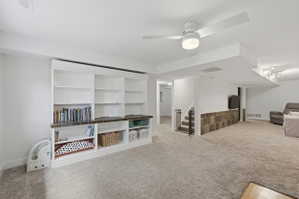 Spacious room featuring extensive built-in shelving, plush carpet flooring, a ceiling fan with integrated lighting, and a partial wall finished with stone-look tile