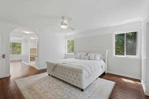 Bedroom with wood-finish flooring, two large windows, a white ceiling fan, and decorative archways leading to an additional space