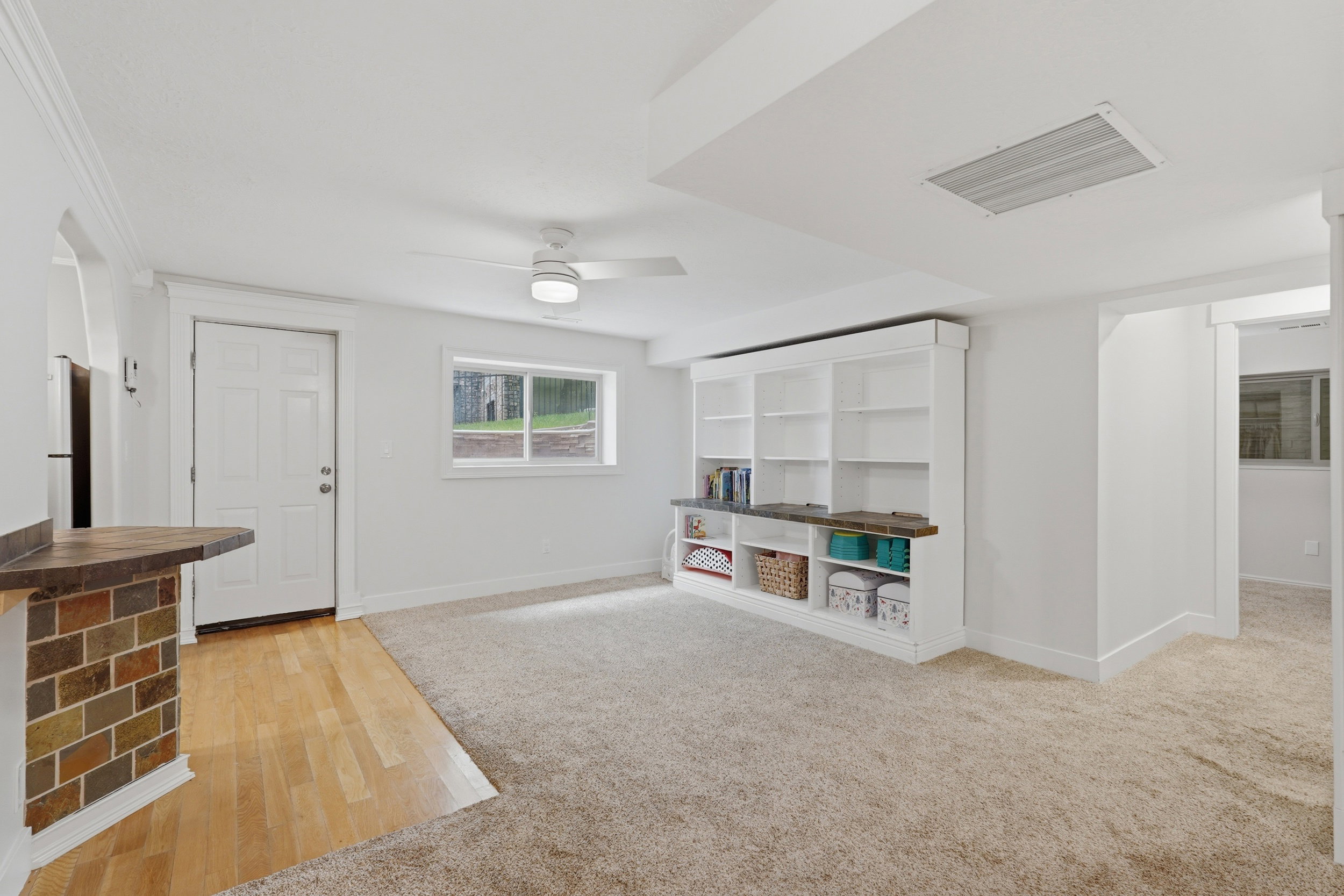 Spacious room featuring plush carpeting, a large built-in shelving unit with a desk area, and a ceiling fan
