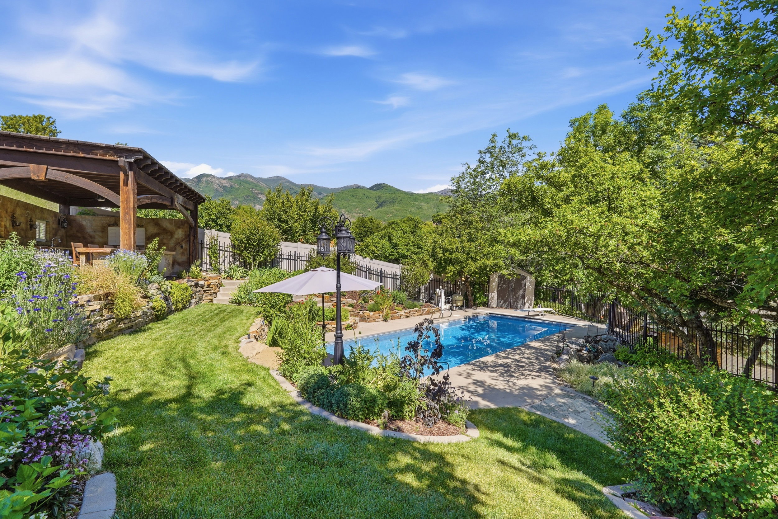 Outdoor swimming pool with surrounding concrete decking, complemented by a stone retaining wall and lush landscaping