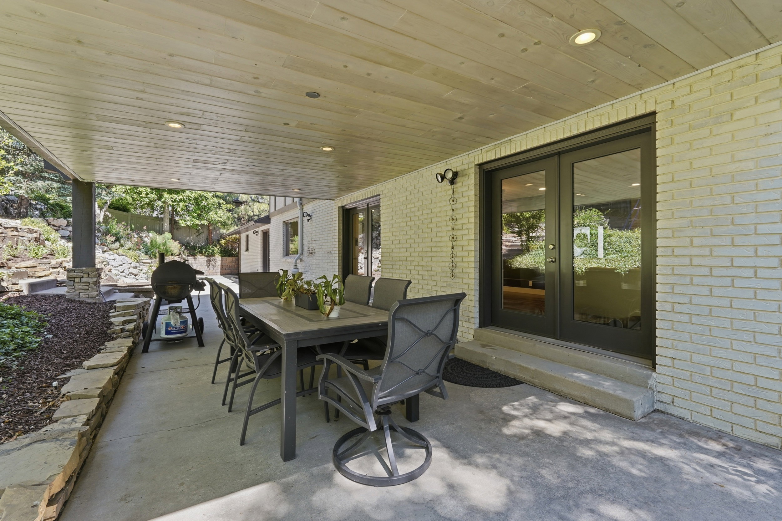 Covered patio featuring a wood-finish ceiling with recessed lighting, concrete flooring, and a stone retaining wall