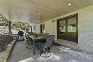 Covered patio featuring a wood-finish ceiling with recessed lighting, concrete flooring, and a stone retaining wall