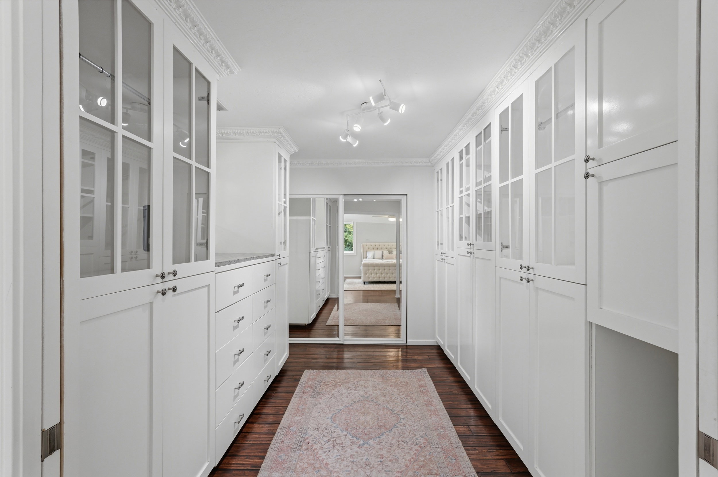 Custom white cabinetry with glass-front uppers, built-in drawers, and dark wood-finish flooring