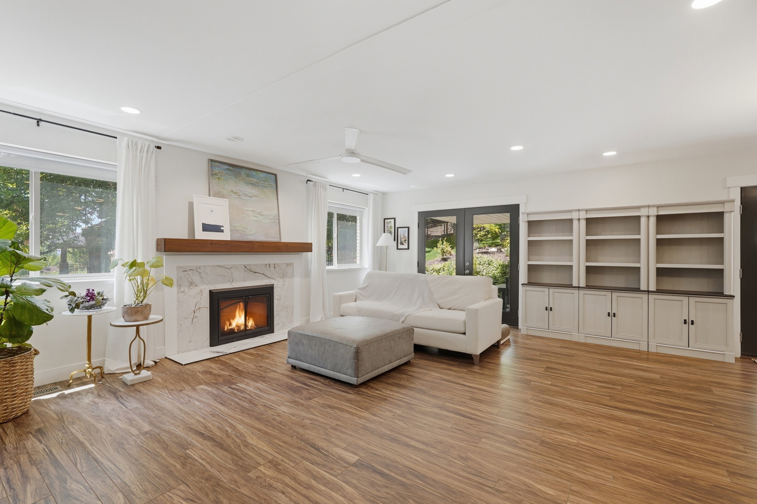 Spacious living area featuring wood-finish flooring, a fireplace with a white stone surround and wood mantel, recessed lighting, and built-in shelving with lower cabinetry