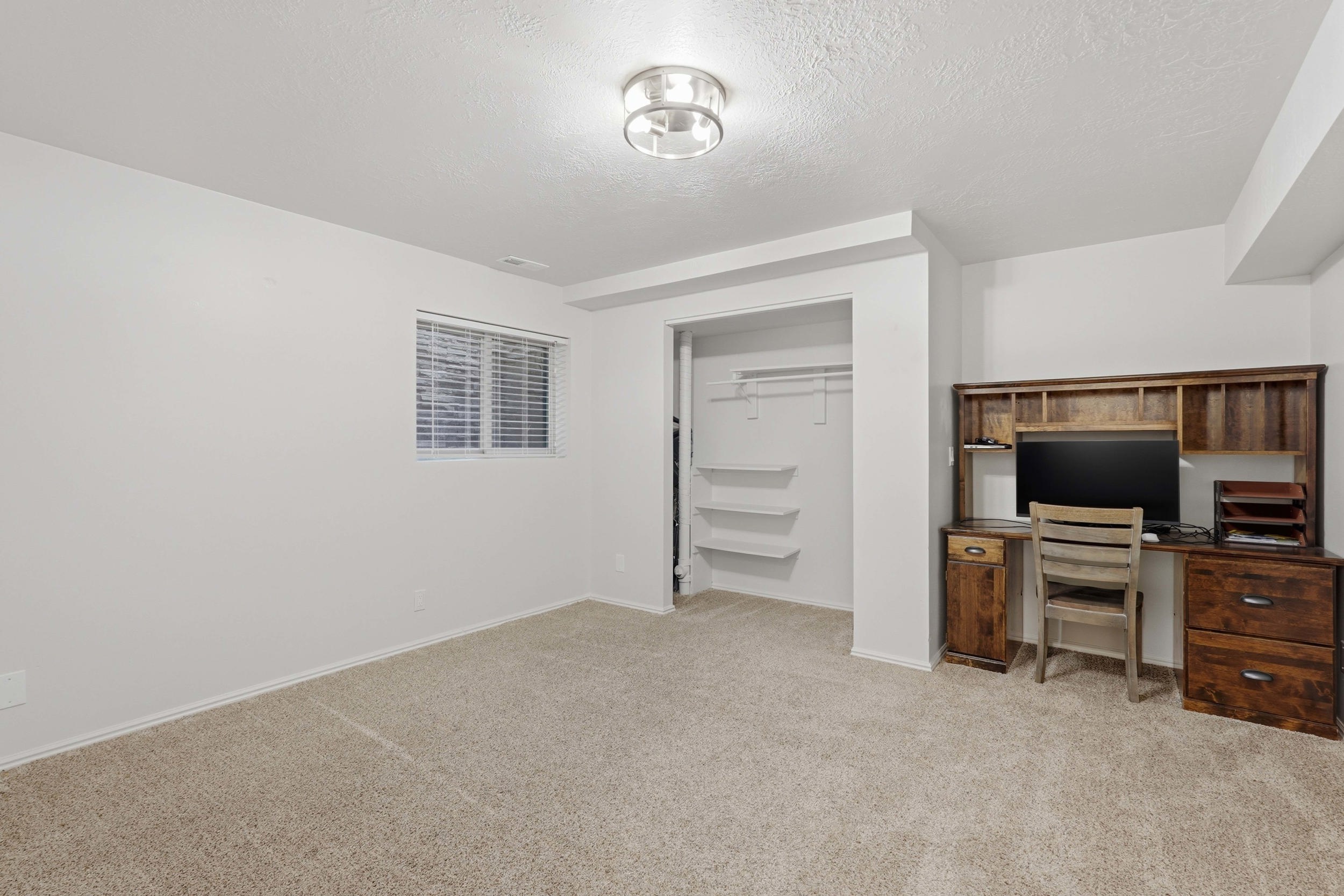 Carpeted room featuring a window with blinds, recessed lighting, and an open closet with shelving and hanging rod