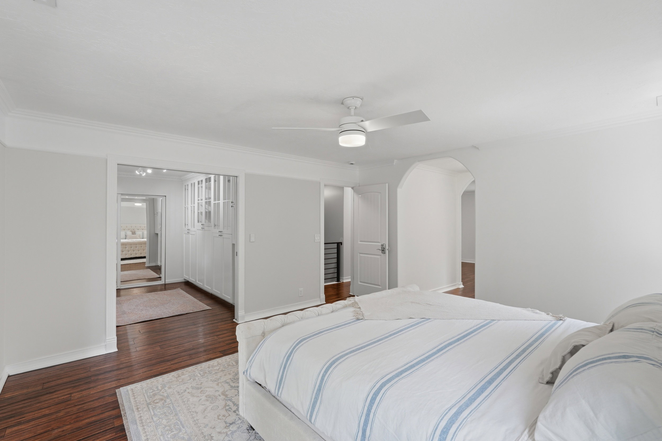Spacious room featuring rich wood-finish flooring, a modern ceiling fan with integrated lighting, and crown molding