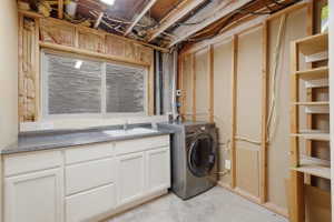 Utility space featuring a single-basin sink, laminate countertop, white cabinetry, and framed unfinished walls